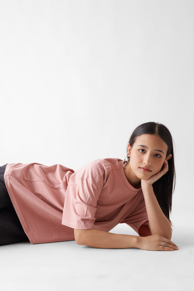 Classic oversized dust pink tshirt for women - laying on the floor with hands on face - unbound crew