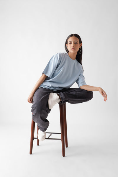 Classic oversized ice blue tshirt for women - sitting on a wooden chair in style - unbound crew