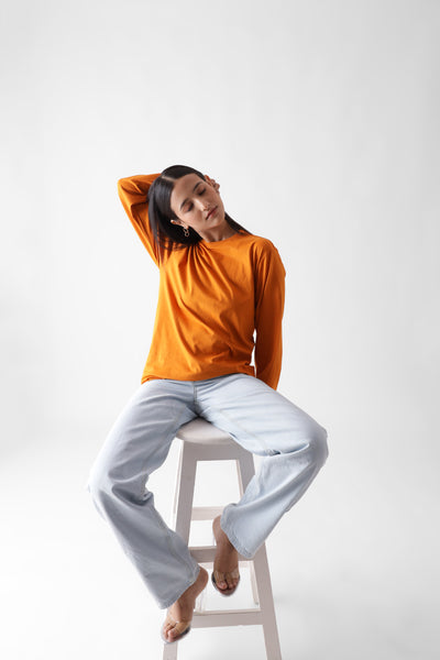 Classic long sleeve orange tshirt for women - sitting on a chair full view - unbound crew